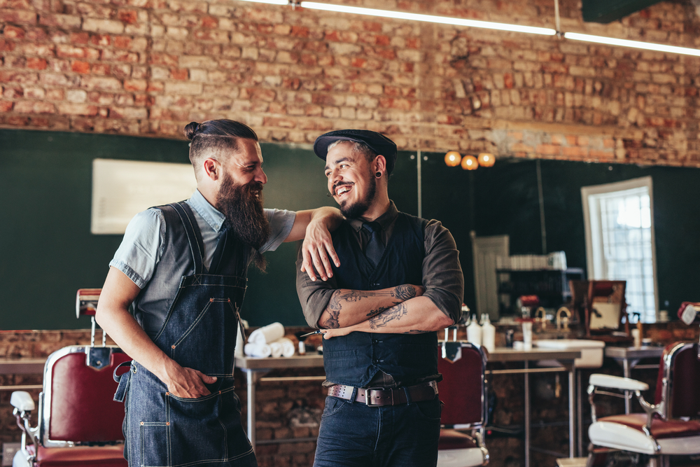 Smiling barber with client standing inside a barbershop